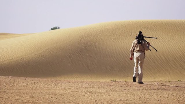Qudra Desert Lake, Dubai, United Arab Emirates - Photographer Walking Alone In The Desert With His Camera And Tripod On A Hot Sunny Weather - Wide Shot