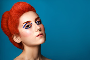 Beautiful girl with colored in red hair and blue eyeliner makeup isolated on blue background