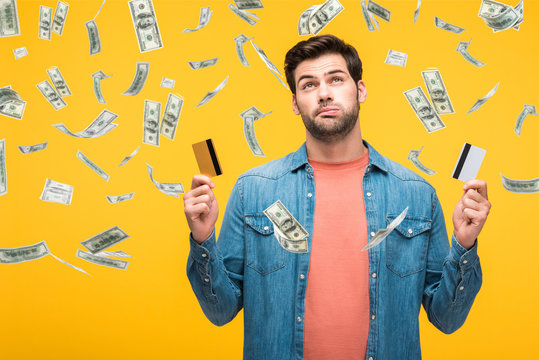 confused handsome man holding credit cards isolated on yellow with money rain illustration