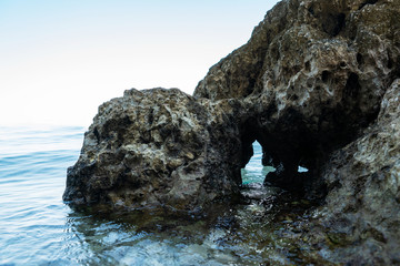 The rocky shore. A fragment of limestone rock in the form of a head with a hole at water level.