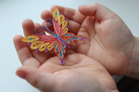 Multicolored quill butterfly in children's hands on white background