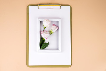 Clipboard with eustoma flower and white frame on beige paper background, flat lay. Post card mockup
