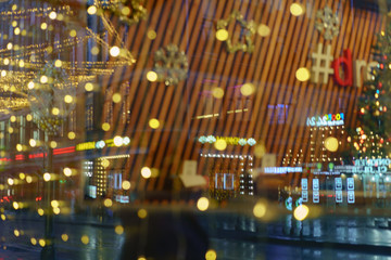 Defocused photography of New Year lights on the city street in night. Christmas mood, festive atmosphere. Suitable as template and background for postcards, greeting cards.