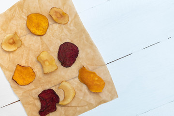 Mixed healthy vegetable chips on cooking paper on white wooden background.
