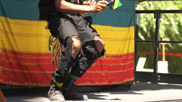 Black man in ripped pants jumping on stage, lion reggae flag behind him, summer festival activity, slow motion shot.