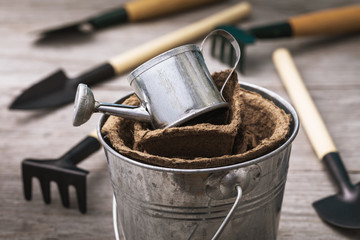 Watering can with peat pots in a bucket surrounded by garden tools, close-up