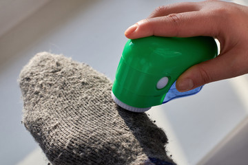 Woman removes lint from wool socks with the help of an electric machine.