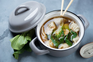 Miso soup with wontons and pak-choi over grey concrete background, studio shot