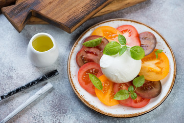 Caprese salad with tomatoes, mozzarella, green basil and olive oil, horizontal shot over beige stone background