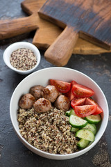Bowl with roasted meatballs, quinoa and vegetables, studio shot over brown stone surface with rustic wooden cutting boards in the background