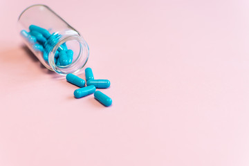 Blue medical capsules in glass transparent bottle on pink pastel background with copy space for your design. Health care concept.