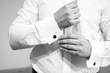 A groom fastening a cuff-link on the shirt black and white