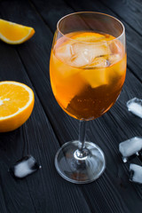 Aperol spritz cocktail in wine glass on the black wooden background. Location vertical. Closeup.