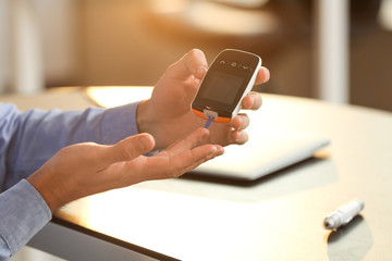 Diabetic man checking blood sugar level in office, closeup