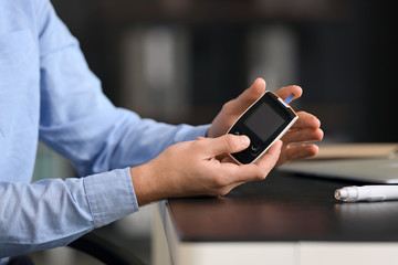 Diabetic man checking blood sugar level in office, closeup