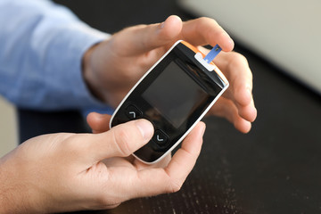 Diabetic man checking blood sugar level in office, closeup