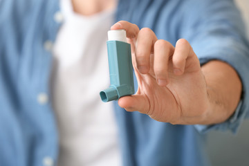 Sick man with asthma inhaler at home, closeup