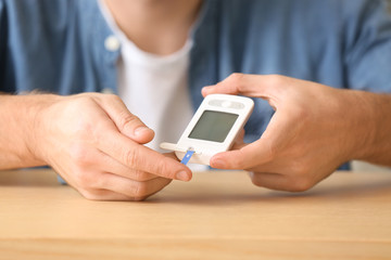 Diabetic man checking blood sugar level at table, closeup