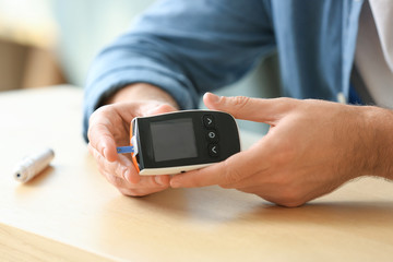 Diabetic man checking blood sugar level at table, closeup