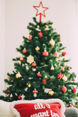 Nice Christmas tree decorated with different colored ornaments next to some cushions with a beautiful and colorful Christmas design - selective focus -