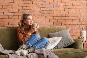 Happy young woman in winter clothes drinking hot chocolate at home