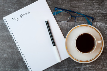 Business concept.Empty sheet of paper with plan. Black coffee, glasses and pen lie near the notebook on a wooden dark background. Top view, flat lay, copy space. Template design card.