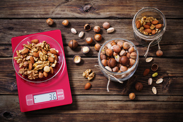 mix of different nuts on  kitchen scale on old wooden background
