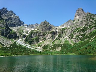 Hidden crystal clear blue green lake in the vast large rocky granite mountains summer sunshine in the high tatras