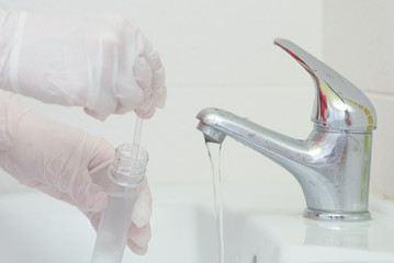 Tap water analysis quality control concept. Hand with a flask and water tap ckose up.