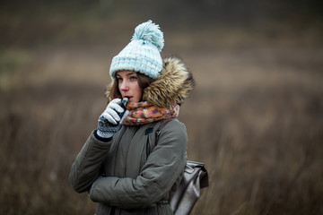 Vaping teenager. Young beautiful white teeage girl in casual clothes smokes an electronic cigarette on the street in the autumn. Electronic cigarette. Deadly bad habit.
