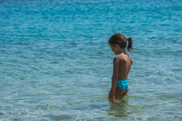 Fototapeta na wymiar Sad little injured girl with bandage on her chin is standing at the water. No possibility to swimming or playing.