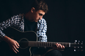 Obraz premium Young Boy Hold Black Guitar on Dark Background