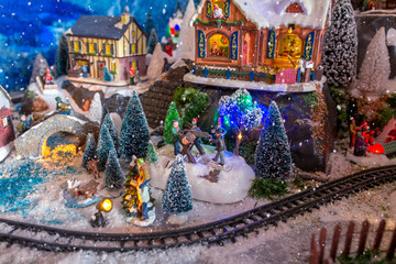 Christmas village. Houses, railway and train, outdoor activities, sleighs, ice skates in a snowy Christmas landscape at night. Christmas tree and snowman. concept for greeting card or postcard