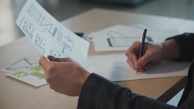Concept of creating new prototype website page. Qualified and successful ux designer working inside modern office with bright and light interior work place. Adult man making notes on drawing blank