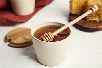 Jar of fresh honey and dipper on white wooden table