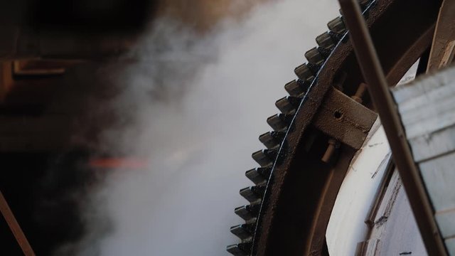 Rotating gear of huge industrial machine, close up. Steam on the background. Rotary kiln on a cement plant. 