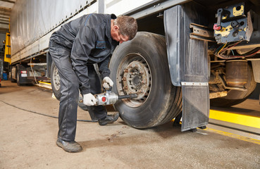 Fototapeta na wymiar Truck repair service. Mechanic works with tire in truck workshop