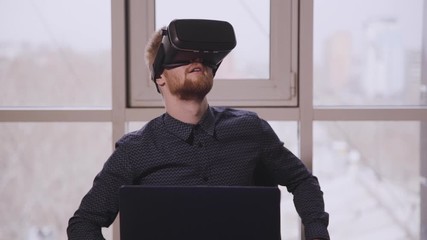 Man executive using virtual reality headset sitting at desk with laptop in office. American businessman researching cyber space, wearing black mask on face during working day in company. Concept - Powered by Adobe