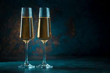 Two elegant romantic glasses with sparkling golden champagne against a dark blue background