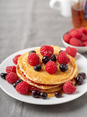 Sweet homemade pancakes with raspberries on white plate.