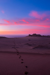 Fußspuren im Sand bei Sonnenuntergang am Meer vor bizarrer Felsküste