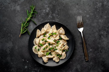 Dumplings - with spices and herbs in a black plate on a stone background. Traditional Russian dish - dumplings