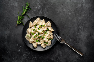 Dumplings - with spices and herbs in a black plate on a stone background. Traditional Russian dish - dumplings