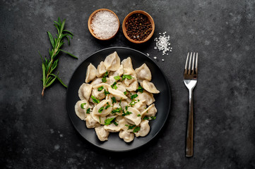 Dumplings - with spices and herbs in a black plate on a stone background. Traditional Russian dish - dumplings