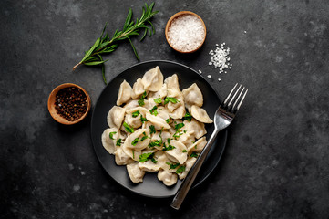 Dumplings - with spices and herbs in a black plate on a stone background. Traditional Russian dish - dumplings