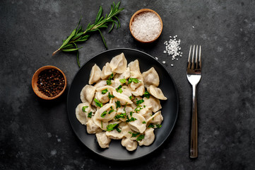 Dumplings - with spices and herbs in a black plate on a stone background. Traditional Russian dish...
