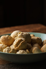 Homemade vegan garlic bread buns made of pizza dough balls filled with herb butter, as side dish, mint green bowl on wooden table, dark background - close-up, angled view, vertical format, copy space