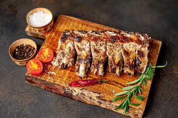 Grilled pork ribs with spices on a cutting board on a stone background 