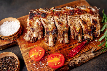 Grilled pork ribs with spices on a cutting board on a stone background 