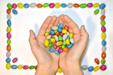 Multicolor candies in hands on white background and colorful frame